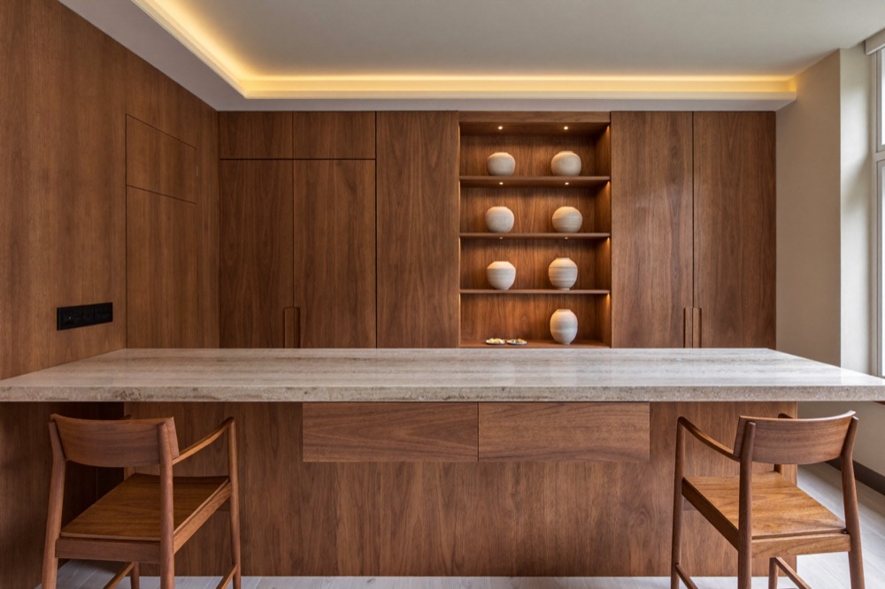 A walnut reception counter with a pale stone top in front of walnut wall panelling and lit shelves of ceramic vessels