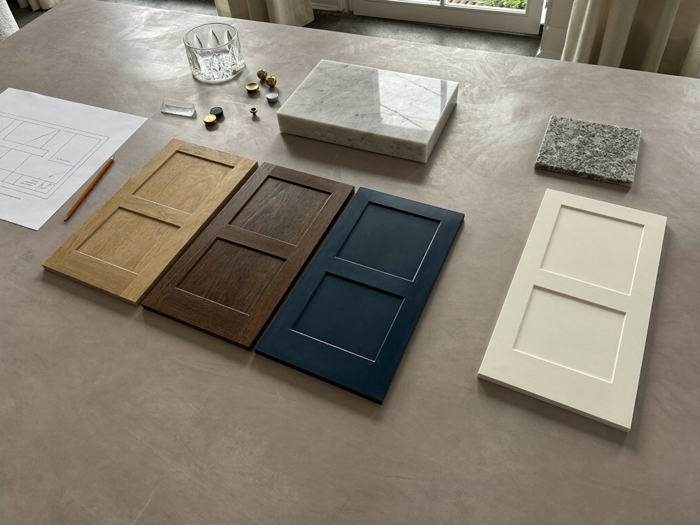 Cabinet door samples in white oak, dark walnut, deep blue and off-white paint beside marble, granite and glass samples
