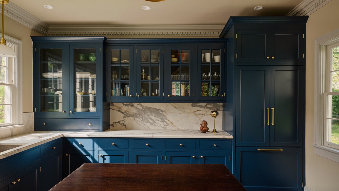 Deep blue painted inset cabinetry with glass-front uppers, brass pulls and a marble backsplash behind a walnut island
