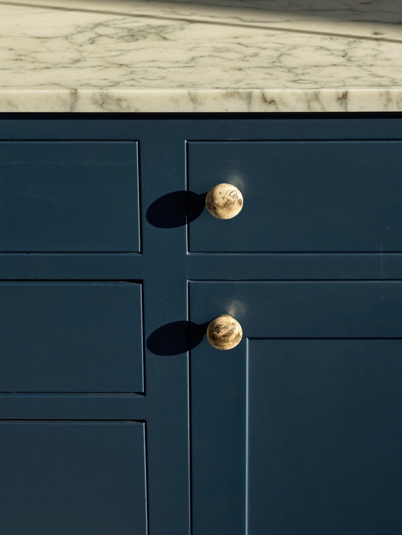 Deep blue painted inset drawer and door fronts with round knobs beneath a white marble counter