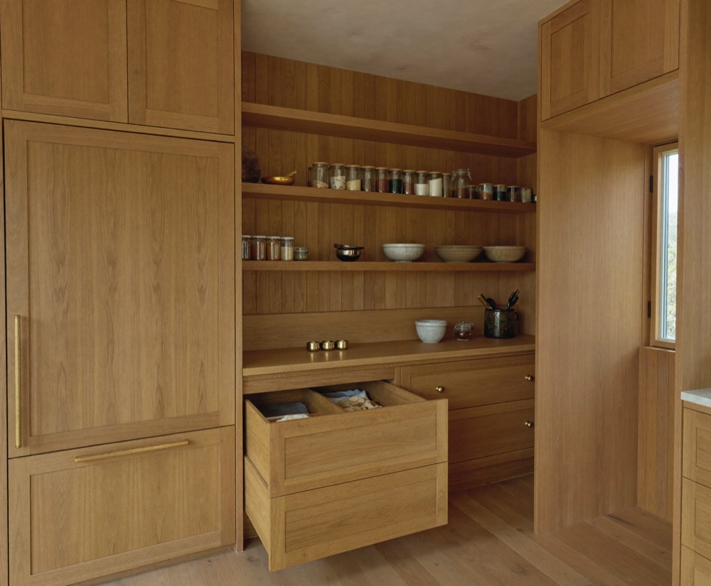 A fitted white oak pantry with open shelves of jars and bowls and a deep drawer pulled out