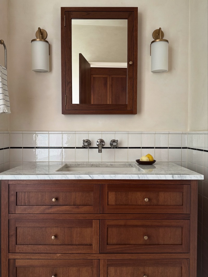 A walnut vanity with a marble top below a matching walnut medicine cabinet and two sconces